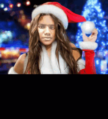 a woman in a santa hat is holding a snowball in front of a christmas tree