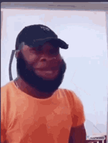 a man with a beard wearing an orange shirt and a black hat .