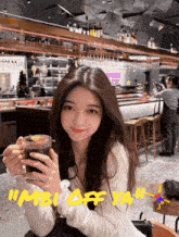a woman is holding a drink in front of a sign that says " imbi off ya "