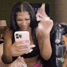 a woman is taking a selfie with her phone while sitting on a bed .