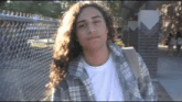 a young man with long curly hair is wearing a plaid shirt and a white shirt