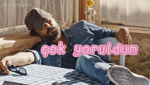 a man with a beard is laying on a table with the words " çok yoruldum " written above him