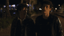 a man in a leather jacket holds another man 's head in his arms