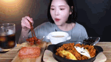 a woman is sitting at a table eating rice with chopsticks