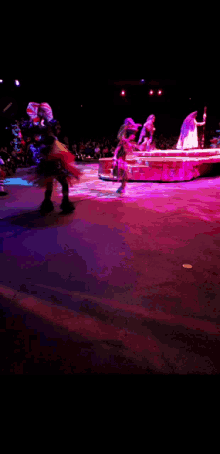 a group of people dancing on a stage with purple lights behind them