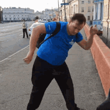 a man in a blue shirt with a backpack on his back is standing on a sidewalk