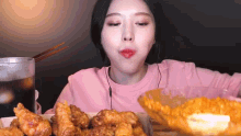 a woman in a pink sweatshirt is eating fried chicken with chopsticks