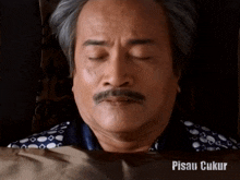 a man with a mustache is laying in bed with his eyes closed and the words pisau ukur written below him