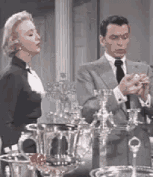 a man and a woman are standing next to each other in front of a table full of silverware