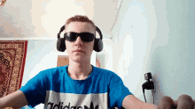 a young man wearing headphones and sunglasses has an adidas shirt on
