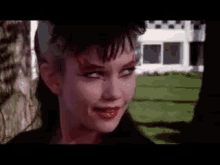 a woman with red makeup on her face is standing in front of a house and looking at the camera .