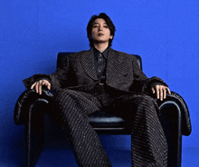 a man in a suit sits in a chair with his hands on the arm rests