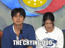 a man and a woman are sitting in front of a microphone with the words the crying duo written above them