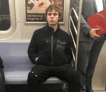 a man is sitting on a subway train with a poster on the wall that says " 2018 trennal through may 27 "