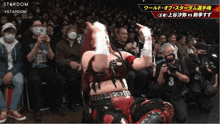 a woman in a red and black outfit is dancing in front of a crowd that is watching a stardom event