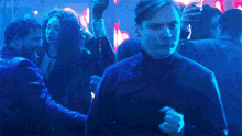 a man stands in a crowd of people holding a glass and a gun with the words elwater2blood visible in the corner