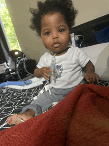 a baby is sitting on a bed holding a bottle