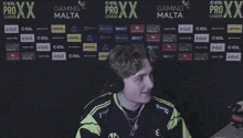 a man wearing headphones in front of a wall that says gaming malta on it