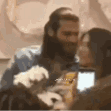 a man with a beard is kissing a woman while holding a phone