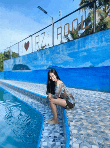 a woman sits on the edge of a swimming pool in front of a sign that says i love rz pool