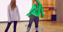 a woman in a green hoodie is standing next to another woman in a gray hoodie .