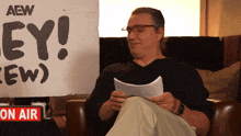 a man is sitting in front of a sign that says aew