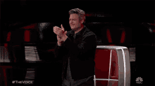 a man applauds in front of a screen that says the voice