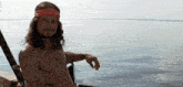 a shirtless man wearing a red bandana with the letters co on it sits in front of a body of water