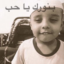 a young boy wearing a white hat is smiling with arabic writing above him