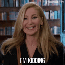 a woman smiles and says i 'm kidding in front of a bookshelf