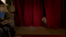 a man is peeking out from behind a red curtain on a stage .