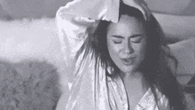 a woman in a robe is laying on a bed with her hand on her head .