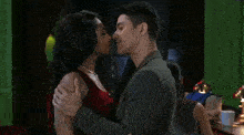 a man and a woman are kissing in front of a green wall