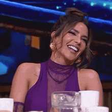 a woman in a purple dress is sitting at a table laughing and smiling .