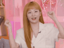 a woman with long blonde hair is wearing a white jacket and holding her hands up in the air .