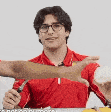 a man wearing glasses and a red shirt is holding a knife over his arm .