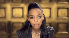 a young girl wearing a leather jacket and a necklace is looking at the camera