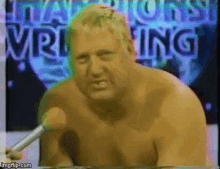 a shirtless man is talking into a microphone in front of a sign that says champions wrestling