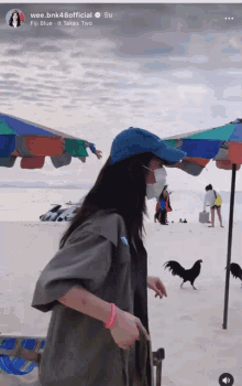 a woman wearing a blue hat and a face mask is walking on a beach