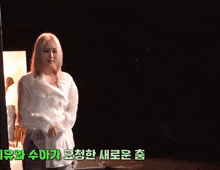 a woman in a white shirt is dancing in a dark room with chinese writing behind her