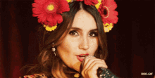 a woman wearing a flower crown singing into a microphone with rbd.gif below her