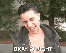 a man in a jacket says okay alright in front of trees