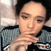 a woman is smoking a cigarette while wearing a plaid sweater with hearts on it .