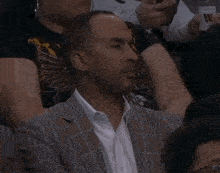 a man in a suit sits in a stadium watching a basketball game