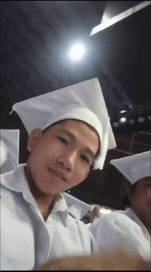 a man in a white cap and gown poses for a photo