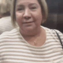 a woman wearing a striped shirt and a necklace is smiling and looking at the camera .