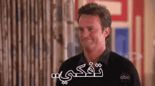 a man in a black shirt is smiling in a room with arabic writing on his face .