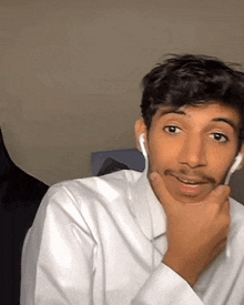 a man wearing a white shirt and ear buds is making a funny face .