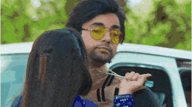 a woman is holding a key to a man 's neck while wearing yellow sunglasses