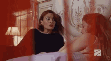 two women are laying on a bed talking to each other .